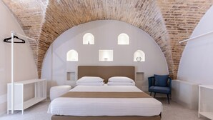 Ein Schlafzimmer mit Ziegeldecke, einem Bett mit weißer Bettwäsche, einem Sessel und einem Kleiderhaken.