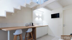 Eine moderne Küche mit einer Holzausziehtheke, zwei Barhocker, einem an der Wand montierten Fernseher und einer Treppe zu einer erhöhten Ebene.