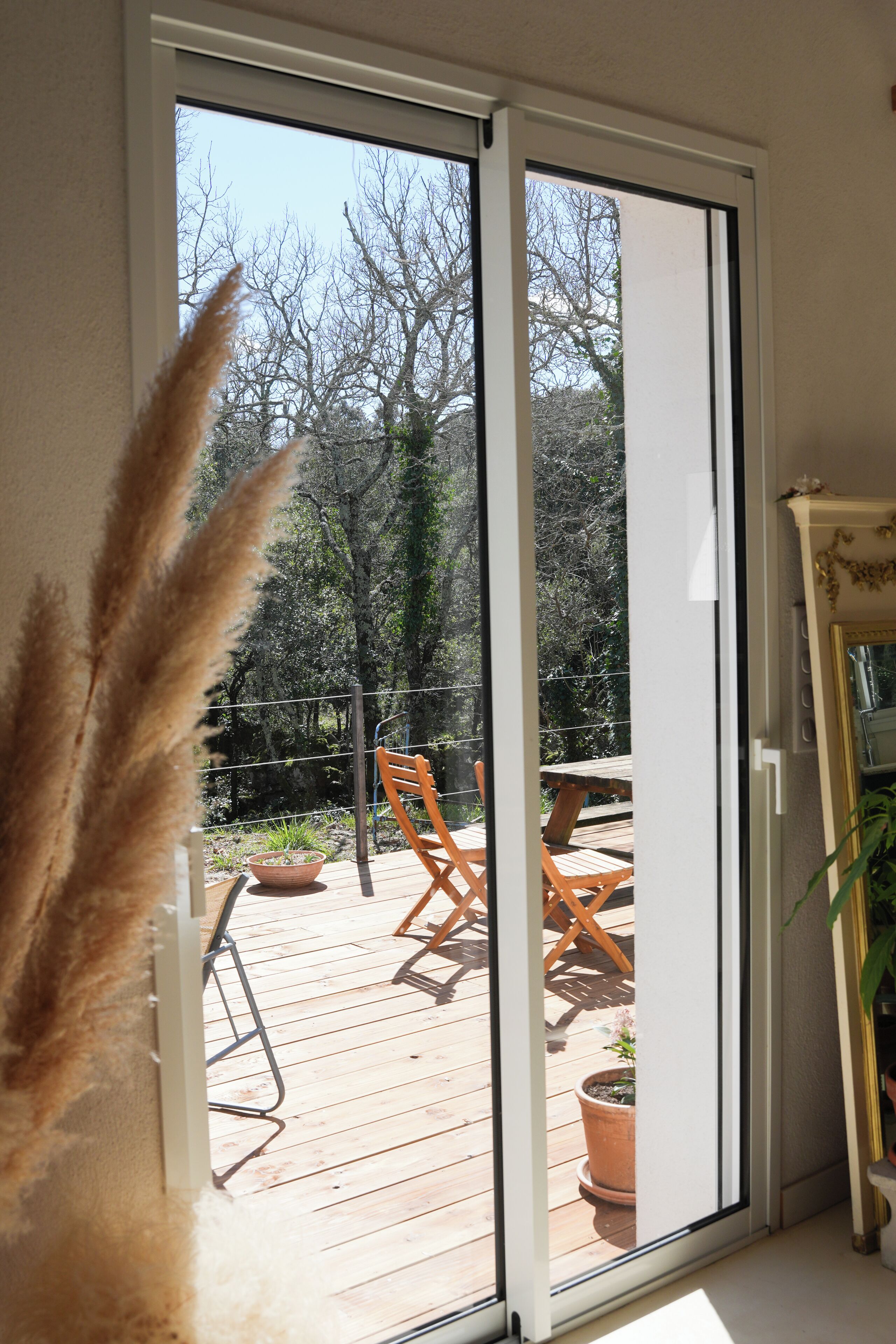 A room with a sliding glass door leading to an outdoor deck with wooden furniture and potted plants.