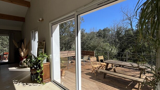 A spacious room with large sliding glass doors leading to an outdoor deck with wooden furniture and plants. - Group holiday in the garrigue - 12 people - total peace and quiet (Saint-Martin-de-Londres)