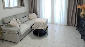 Uma sala de estar moderna com um sofá cinzento, uma mesa de centro redonda e uma mesa lateral preta com um vaso.