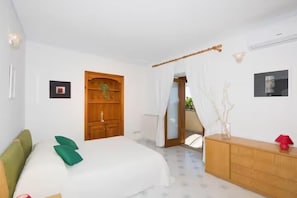 A bedroom with a bed, a wooden wardrobe, a bedside table, and a view of the outside. - De Vivo Realty - Villa Savina Positano (Positano)