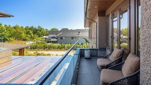 Varanda com guarda-corpo de vidro, área de estar ao ar livre e vista para as casas vizinhas.