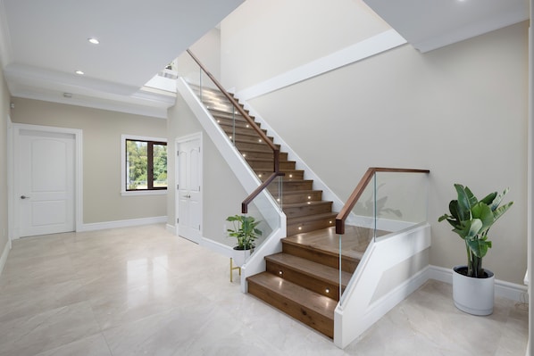 A modern staircase with glass railings, wooden steps, and potted plants.