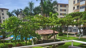 A balcony with a view of a pool, greenery, and a building with multiple floors. - Family-friendly Condo With Pool View, Walk to Jaco Beach (Jacó)