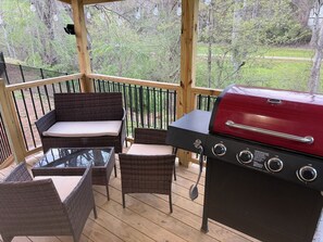 A covered outdoor area with wicker furniture, a glass table, and a red barbecue grill. - Delightful 3-bedroom home with a fenced in yard in Leicester (Leicester)