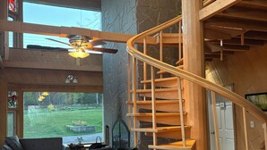 A spacious living area with a wooden staircase, a ceiling fan, and a large window offering a view of the outdoors. - Stunning Lakehouse in Castle Danger (Two Harbors)