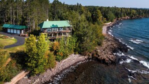 A coastal property with a large building featuring multiple decks, surrounded by dense forest and a rocky shoreline. - Stunning Lakehouse in Castle Danger (Two Harbors)