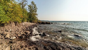 A rocky shoreline with trees and a clear view of the water. - Stunning Lakehouse in Castle Danger (Two Harbors)