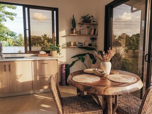 A kitchen with a window, wooden cabinets, wicker chairs, a round wooden table, and potted plants. - Private Villa with Pool & Nature (Parrita)