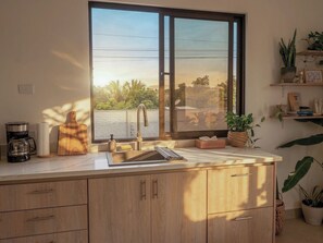 A kitchen with a large window, wooden cabinets, a coffee maker, and a cutting board. - Private Villa with Pool & Nature (Parrita)