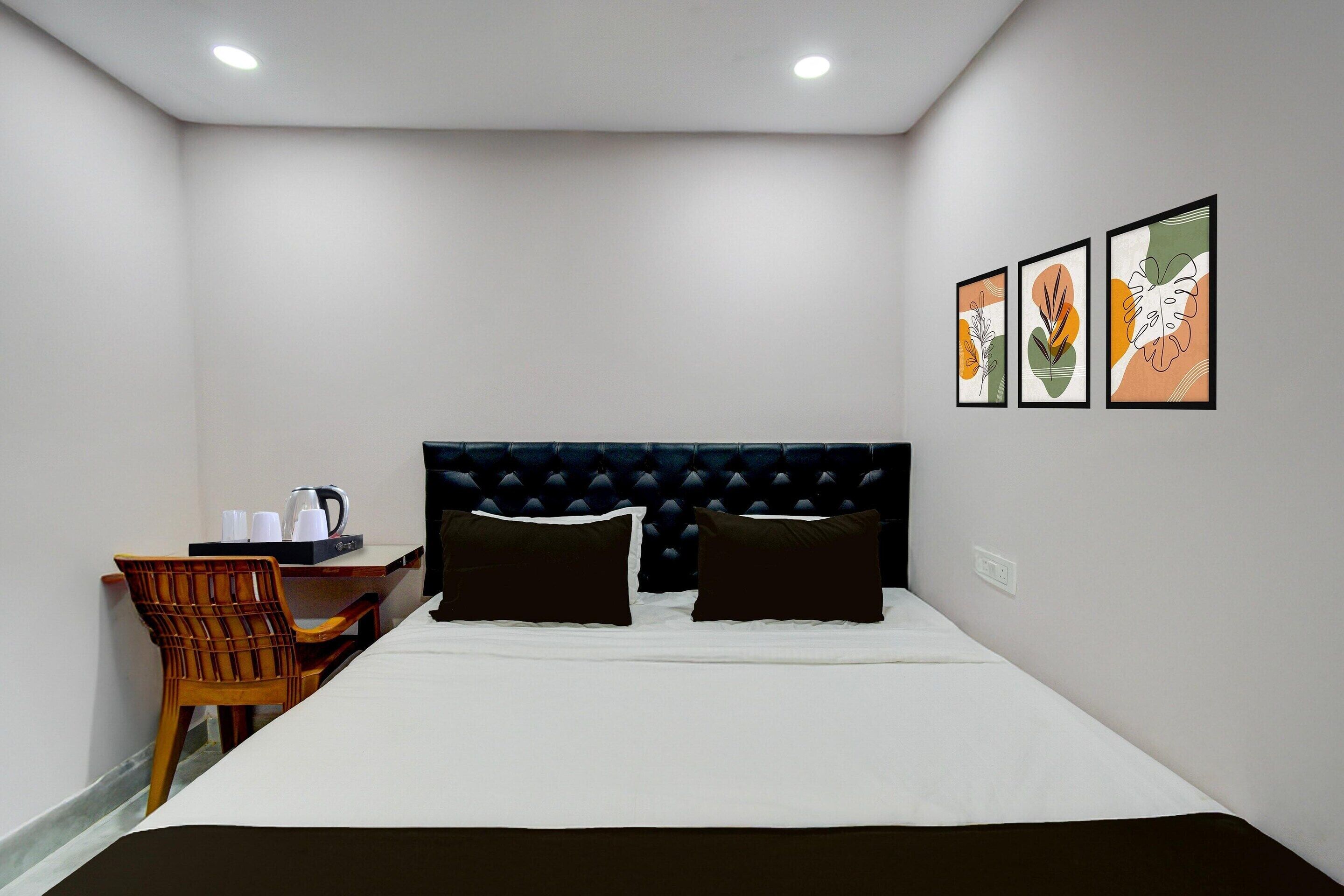 Ein Hotelzimmer mit Bett, Schreibtisch mit Wasserkocher, Stuhl und drei gerahmten Kunstwerken an der Wand.