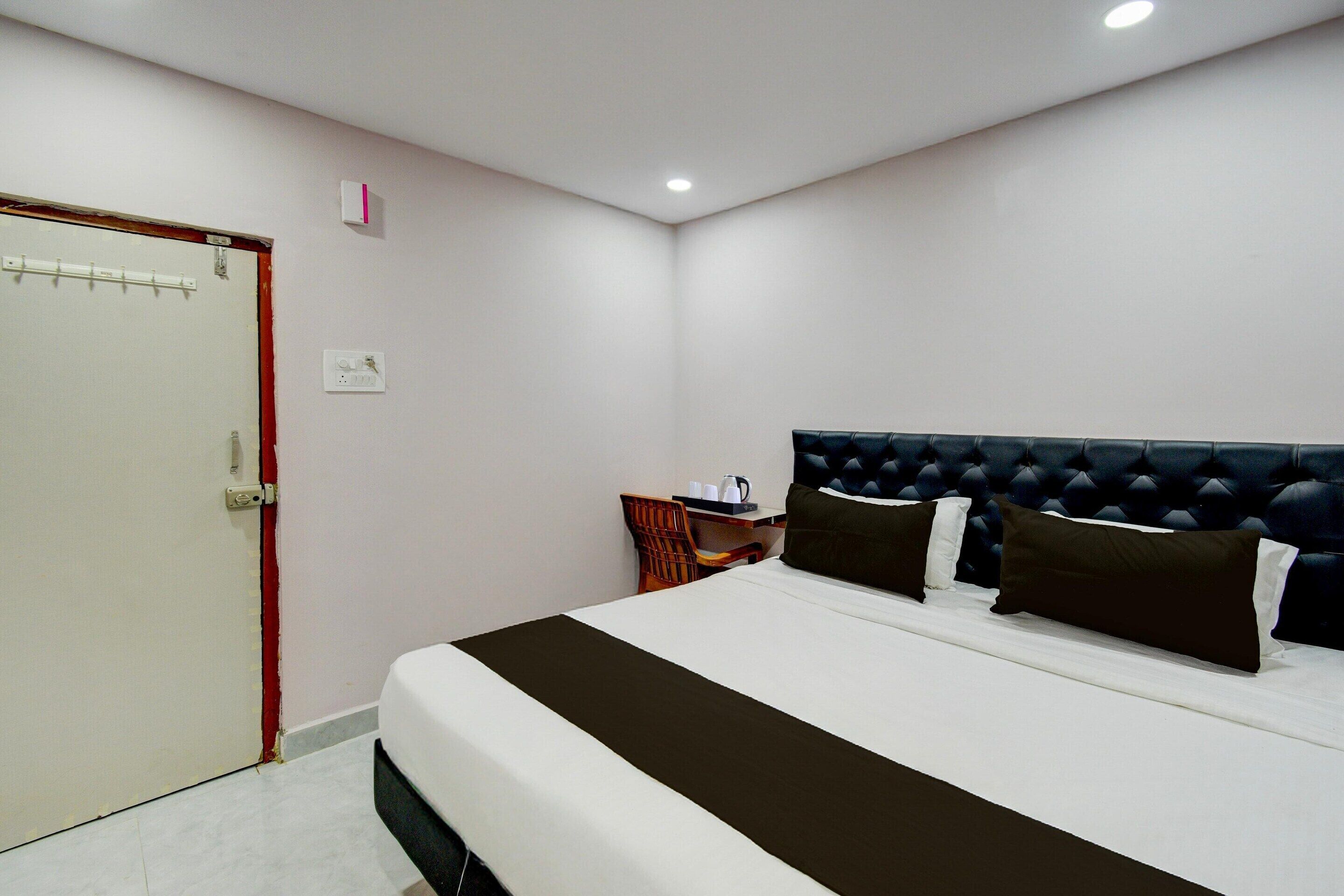A hotel room with a bed, a chair, a small table, and a door.