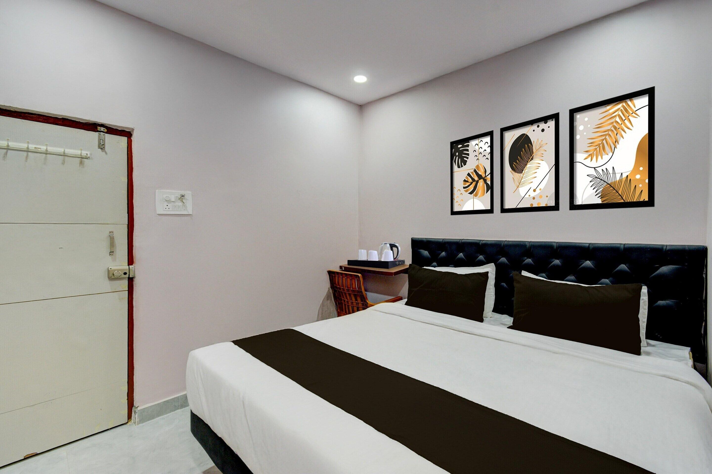 A hotel room with a bed, a nightstand, a chair, and three framed artworks on the wall.