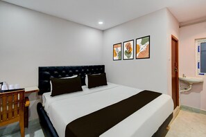 A hotel room with a bed, a wooden chair, a bedside table, a wall-mounted sink, and framed artwork. - Hotel O Injapur Lake (Hyderabad)