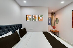 A hotel room with a large bed, a small table with a vase, and three framed artworks on the wall.