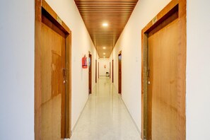 A long, narrow hallway with wooden doors on both sides, a fire extinguisher on the left wall, and a ceiling with a wooden panel design.