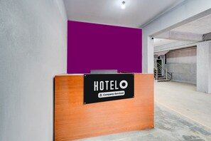 A reception desk with a sign that reads 'HOTELO Company-Serviced' in a modern lobby with a concrete floor and a purple accent wall.