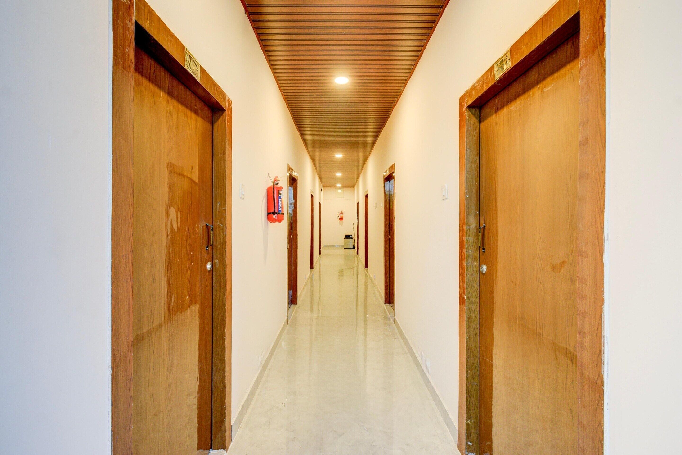 Un couloir avec des portes en bois, un extincteur et un plafond doté d’un éclairage encastré.