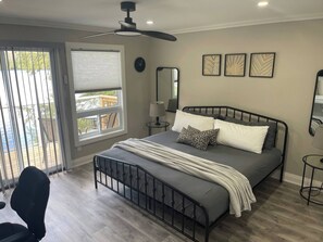 A bedroom with a bed, a ceiling fan, a window with blinds, a bedside table, and a chair. - Luxury Waterfront Retreat in Highlands East - Ridgestone Cottage (Highlands East)