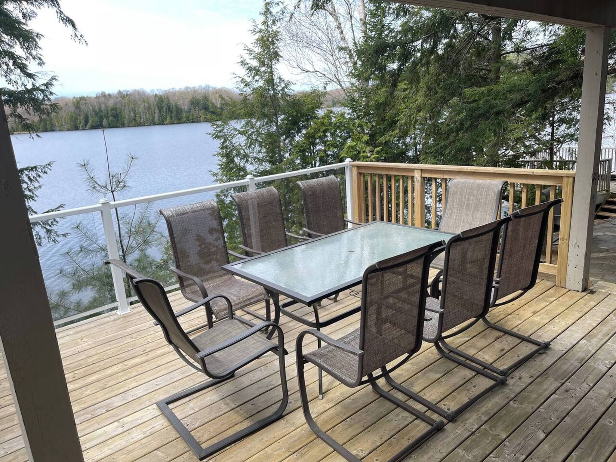 Une terrasse avec une table et des chaises en verre, donnant sur un lac.