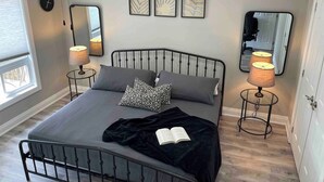 Une chambre à coucher comprenant un lit, deux lampes de chevet, un ventilateur de plafond, un grand miroir et trois œuvres d’art murales.
