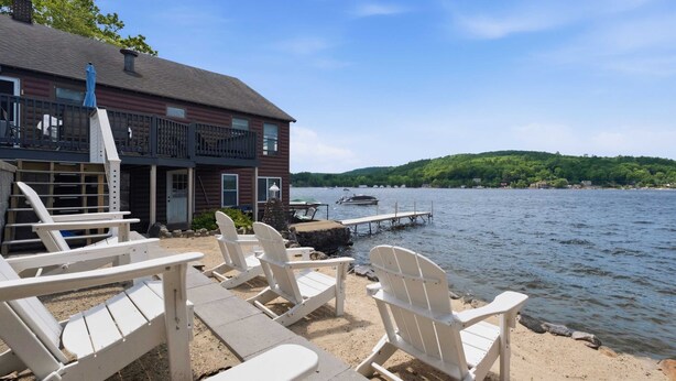 Une terrasse au bord du lac, dotée de chaises Adirondack, un quai et un bâtiment avec un balcon.