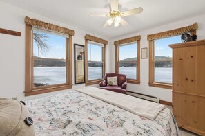 A bedroom with a large bed, a ceiling fan, and a view of a snowy landscape through multiple windows.