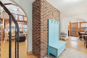 A room with a brick wall, a blue bench, a wooden staircase, and a dining area with a table and chairs.