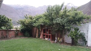 A grassy yard with a brick wall, a small structure with a red roof, and a mountain in the background. - Tampu Wasi Luci (Distrito de Coya)
