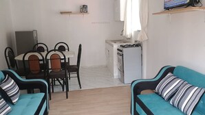 A compact living space with a dining area, kitchenette, and two sofas with striped pillows. - Tampu Wasi Luci (Distrito de Coya)