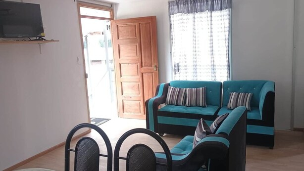 A living room with a sofa, two chairs, a TV, a door, and a window with curtains. - Tampu Wasi Luci (Distrito de Coya)