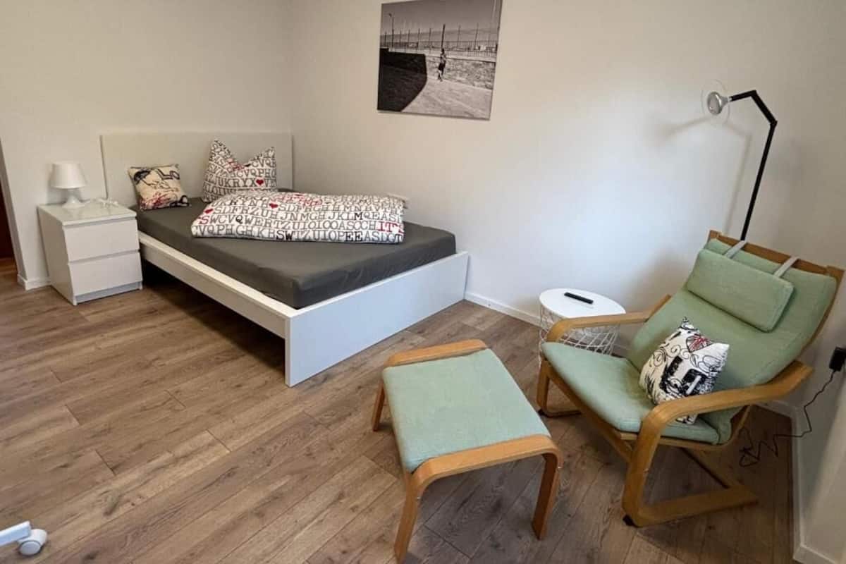 A bedroom with a bed, bedside table, chair, and a small stool.