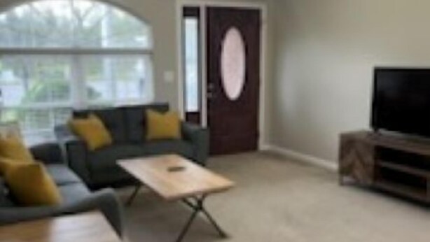 Un salon comprenant un canapé, une table basse, un meuble pour la télévision et une porte dotée d’une fenêtre ronde.