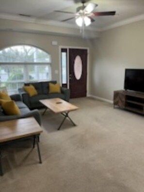 Een woonkamer met een bank, salontafel, tv-meubel en een deur met een rond raam.