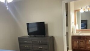 Une chambre à coucher comprenant un lit, une commode, un téléviseur et un ventilateur de plafond.