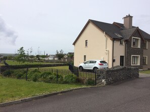 A residential house with a stone wall, a parked car, and a grassy area with a fence. - STRUTHAN BEAG DINGLE (Dingle)