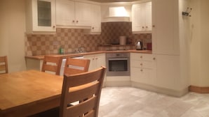 A kitchen with white cabinets, a tiled backsplash, a dining table with chairs, and a built-in oven. - STRUTHAN BEAG DINGLE (Dingle)