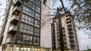 Um edifício moderno de vários andares com varandas, grandes janelas e um letreiro indicando espaços comerciais à venda.