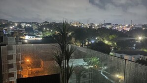 Um edifício alto com varanda de vidro que dá para a paisagem urbana à noite.
