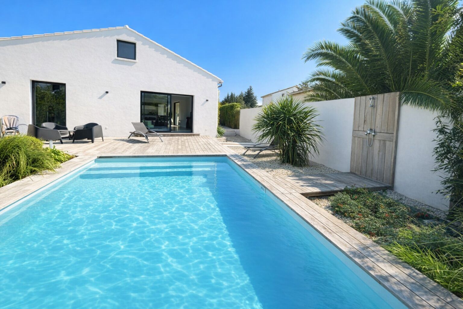 A modern house with a swimming pool, outdoor seating, and a wooden fence.