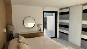 A bedroom with a bed, bedside lamp, round mirror, and a view of the outside through a sliding door. - Private cocoon & swimming pool Absolute calm (Rognonas)