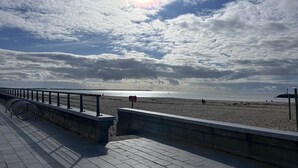 En strandpromenad med ett räcke, en strand i bakgrunden och en klar himmel.