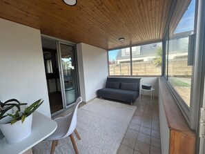 Ein modernes Zimmer mit einem grauen Sofa, einem weißen Sessel, einem kleinen Tisch mit Topfpflanze und Blick auf ein Haus durch große Fenster.