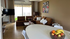 Ett hotellrum med en soffa, ett matbord med frukt, en tv och en tavla på väggen.
