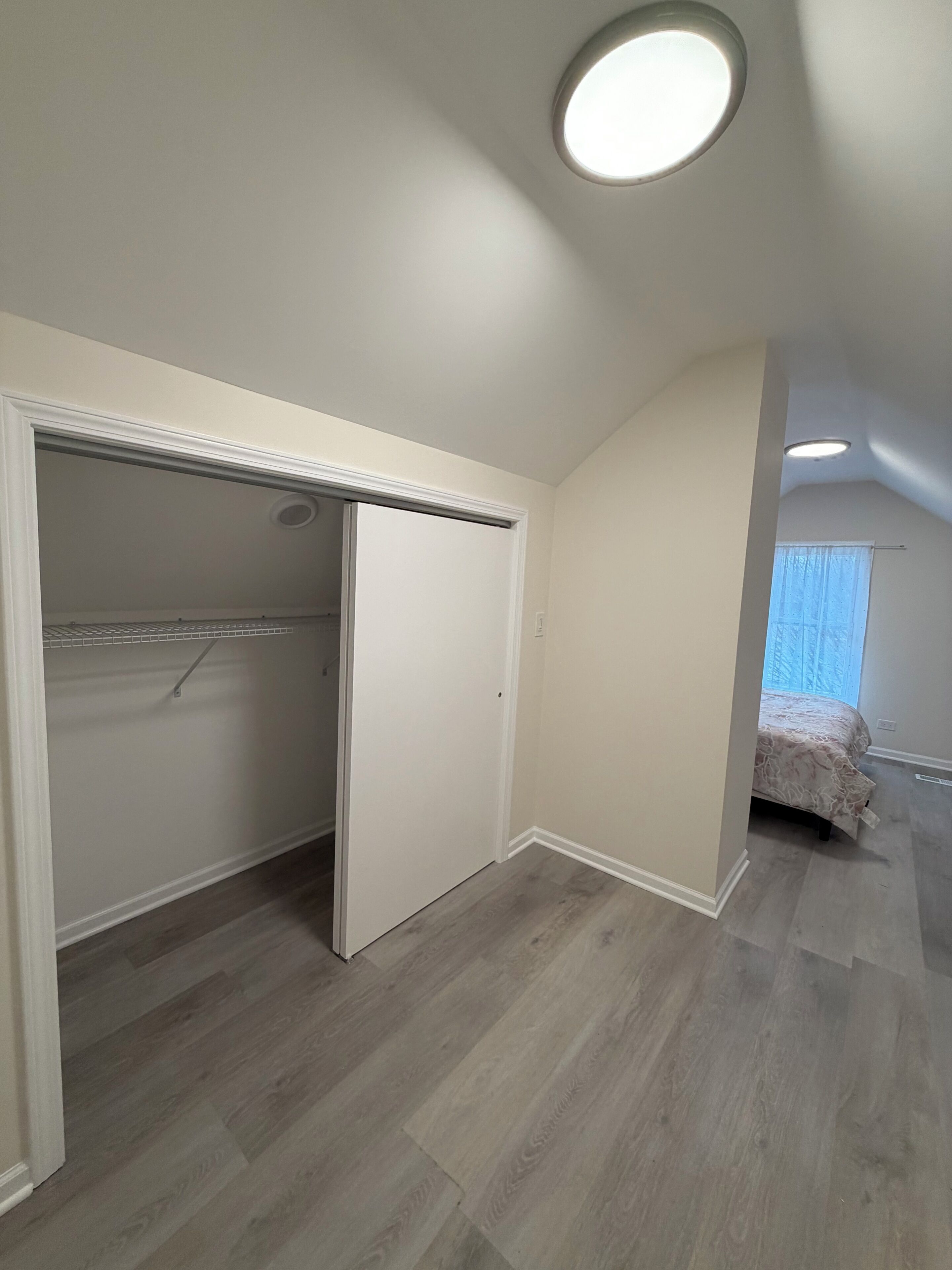 Quarto com closet espaçoso, cama e luminária no teto.