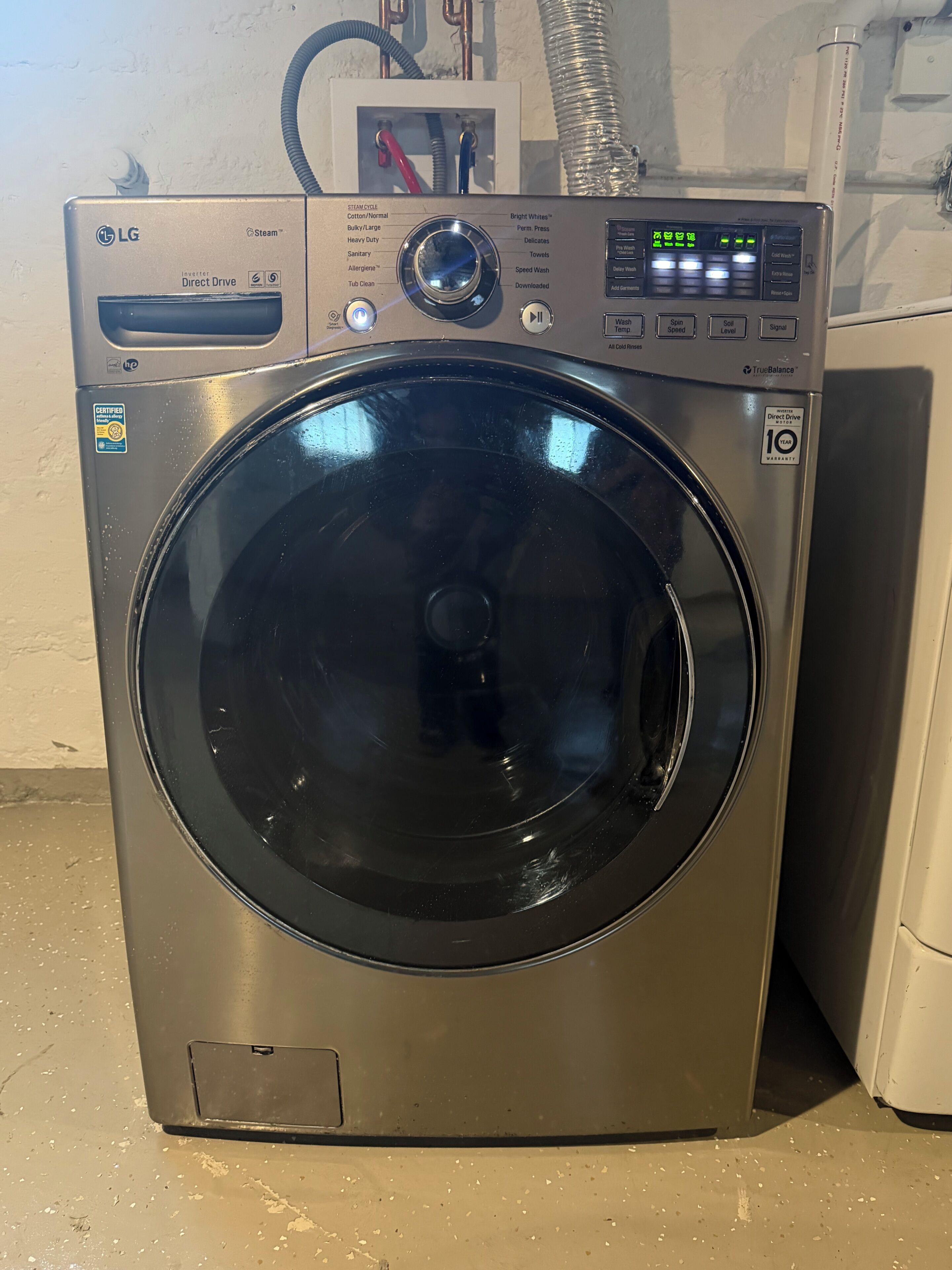 Une laveuse LG à chargement frontal, à vapeur, dotée d’un panneau de commande, d’étiquettes de certification et d’un autocollant de garantie.