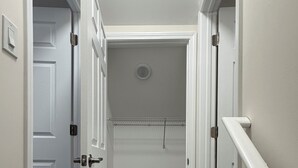 Un pasillo estrecho con puertas blancas, piso de madera y un armario con barra metálica.