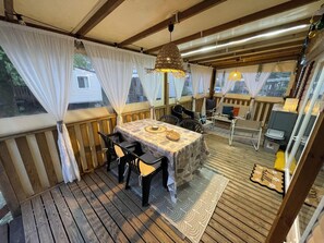 A covered outdoor deck with a table and chairs, wooden railings, and a ceiling with exposed beams.