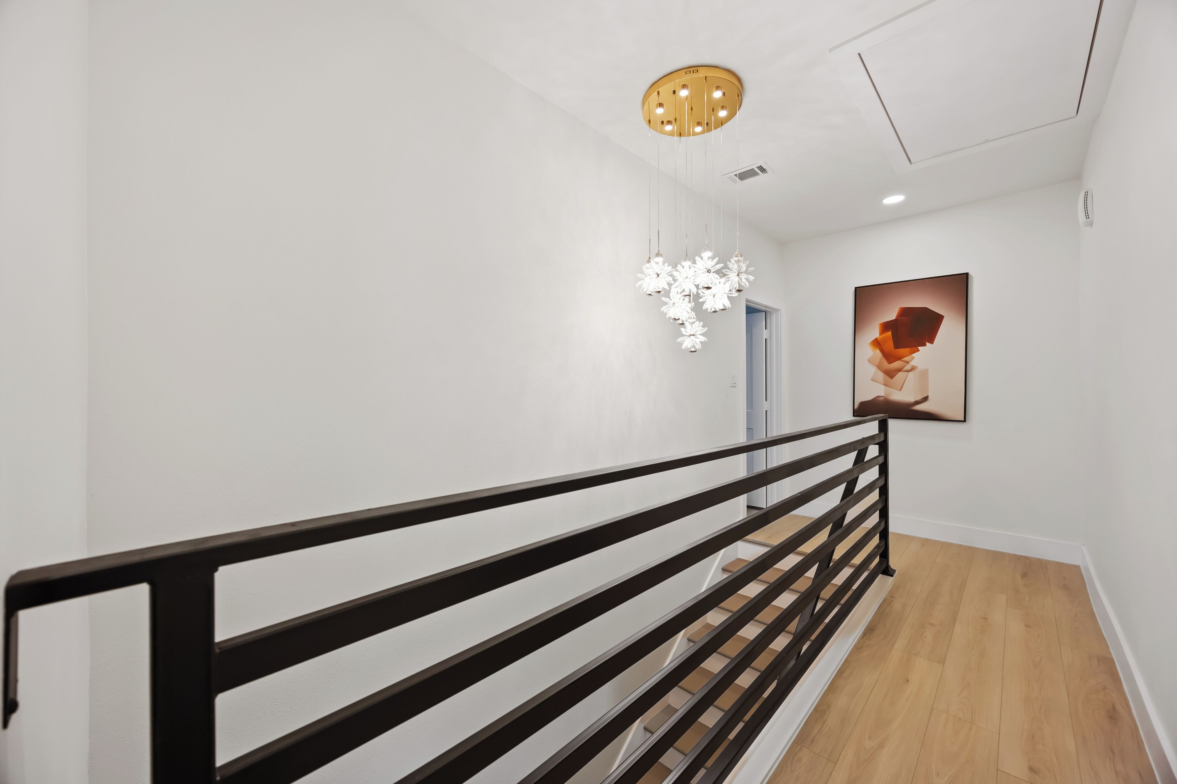 A modern interior with a wooden staircase, a black railing, a hanging light fixture, and a framed artwork on the wall.